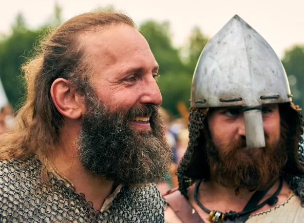 Two men in viking reenactment costumes, one with a helmet, smiling and enjoying the event